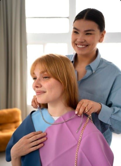 A smiling woman tries on a necklace while another woman fastens it for her
